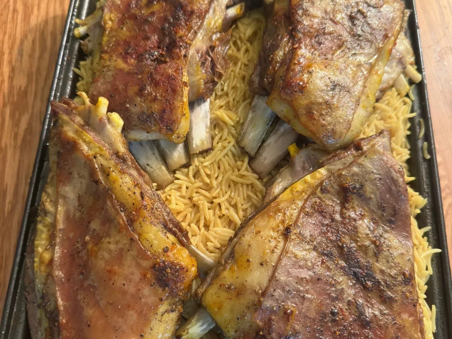 A tray of slow-roasted lamb pieces on golden spiced rice and vermicelli