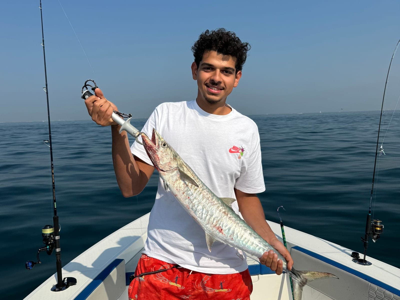 Youssef on a boat at sea, smiling and holding up a long silver fish he caught