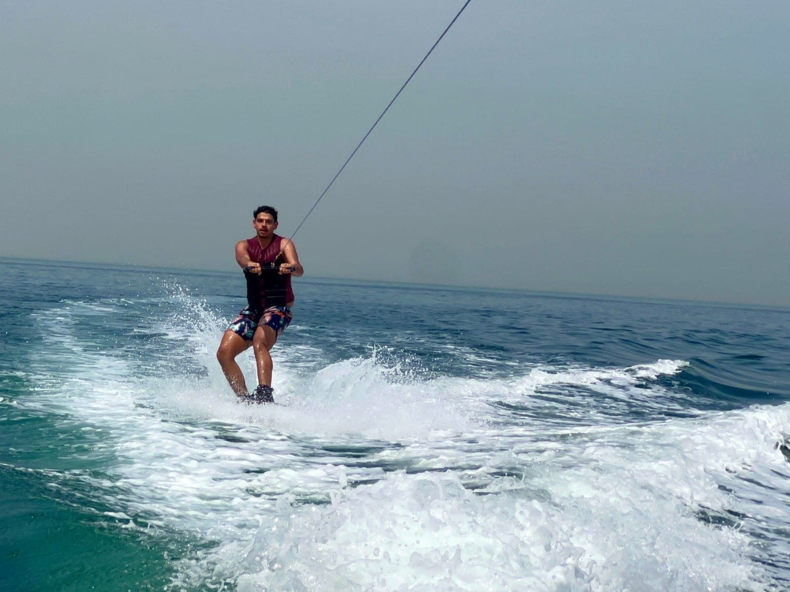 Youssef wakeboarding behind a boat, holding the tow rope as spray flies off the wake